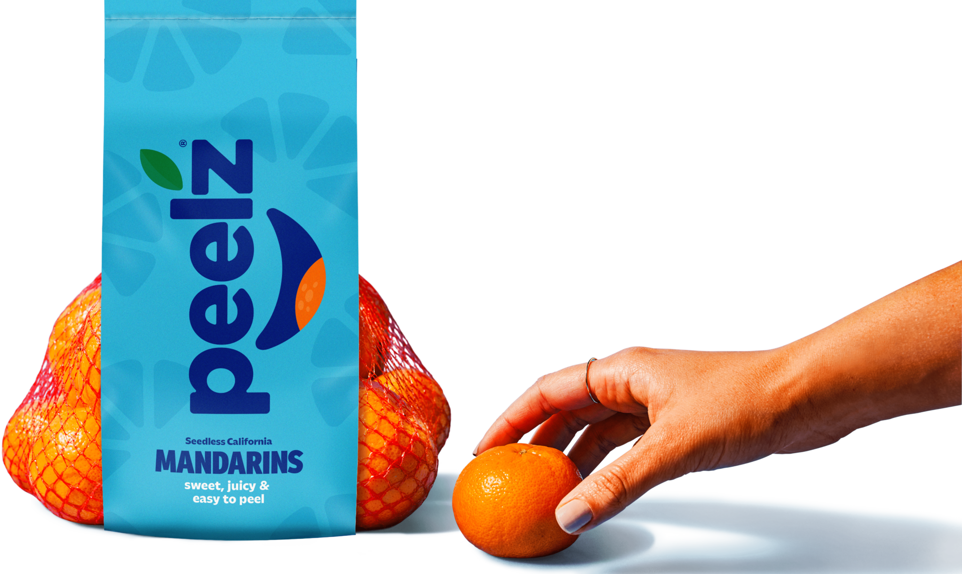 Hand reaching for a Peelz mandarin orange, next to a bag of Peelz seedless California mandarins