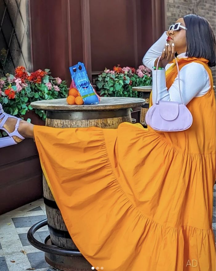 A woman in an orange dress in front of a barrel with a bag of Peelz mandarin oranges.