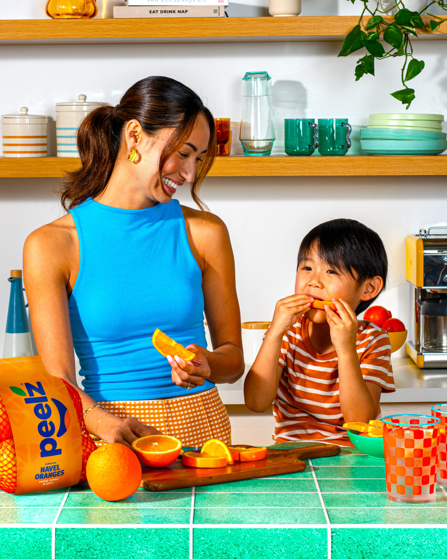 A woman and child in a kitchen eating sliced Peelz navel oranges