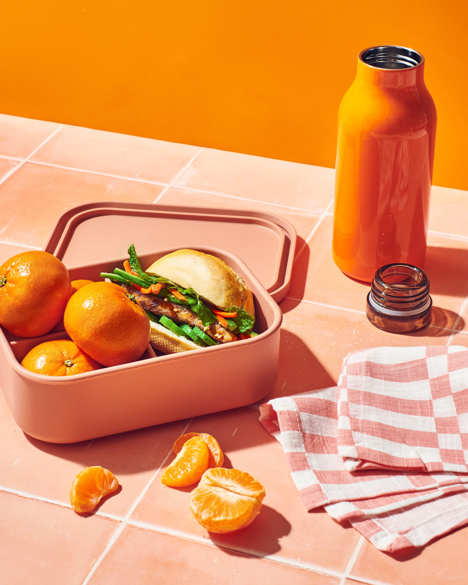 A lunch box with Peelz mandarin oranges next to a sandwich and a peeled mandarin orange.